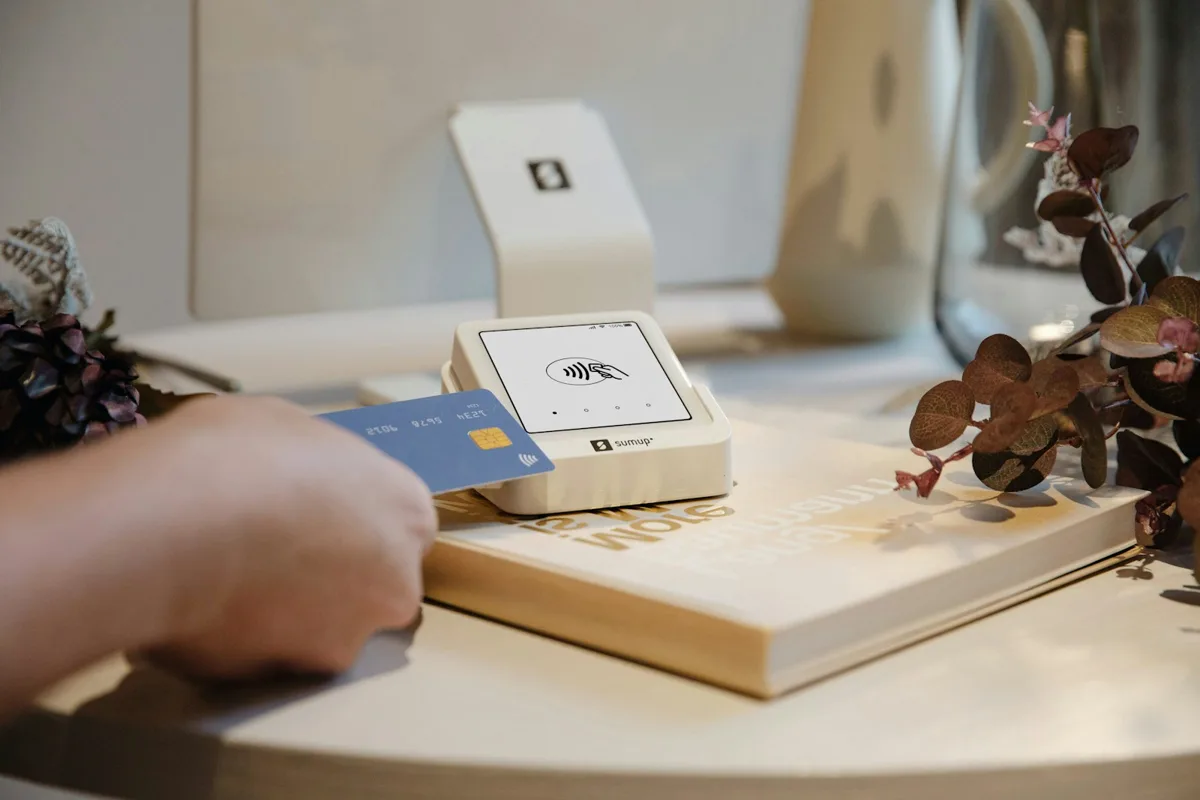 A hand holding a payment card beside a SumUp card reader on a counter.